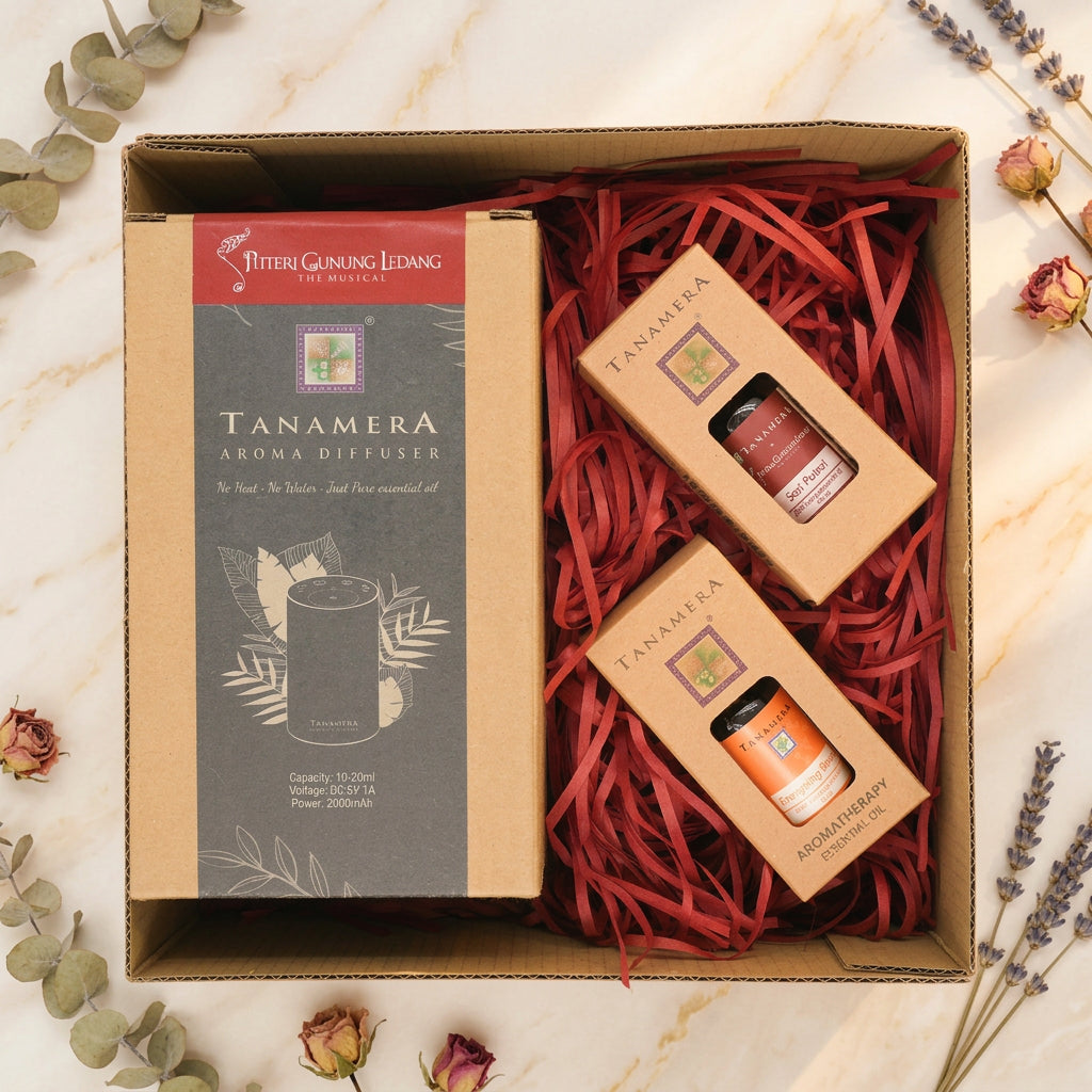 A boxed gift set from Four Grass Living featuring a Tanamera aroma diffuser and two small essential oil bottles, arranged in red paper shred inside a brown cardboard box on a light gray background.