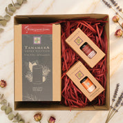 A boxed gift set from Four Grass Living featuring a Tanamera aroma diffuser and two small essential oil bottles, arranged in red paper shred inside a brown cardboard box on a light gray background.