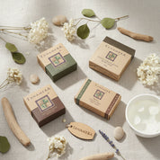 A Tanamera gift box containing four bars of formulation body soap in different colors (green, white, black, and brown) nestled in pink shredded paper inside a cardboard box.