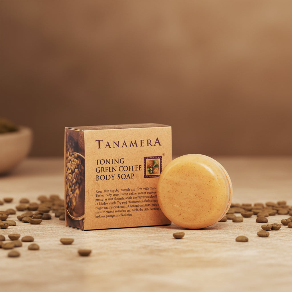 Tanamera Toning Green Coffee Body Soap shown with its kraft paper box, placed on a wooden surface with scattered coffee beans. The round soap bar is a warm golden-beige color, and the box is brown with black text and coffee bean imagery.